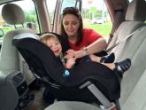 Woman depicted properly hooking her young child's safety seat into the back of her SUV